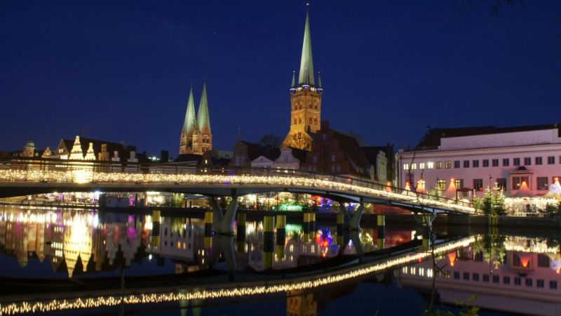 Julmarknad Lbeck med upplyst bro och historiska kyrktorn mot kvllshimlen.