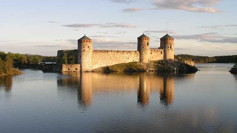 Savonlinna i solnedgång – silhuetten av Olavinlinna slott och stadens öar speglas i sjön Saimaa
