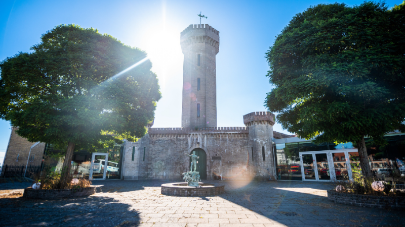 Vattenborgen i Karlskrona, historisk byggnad med torn och borgliknande murar, font�n i f�rgrunden och gr�nskande tr�d under en solig dag.