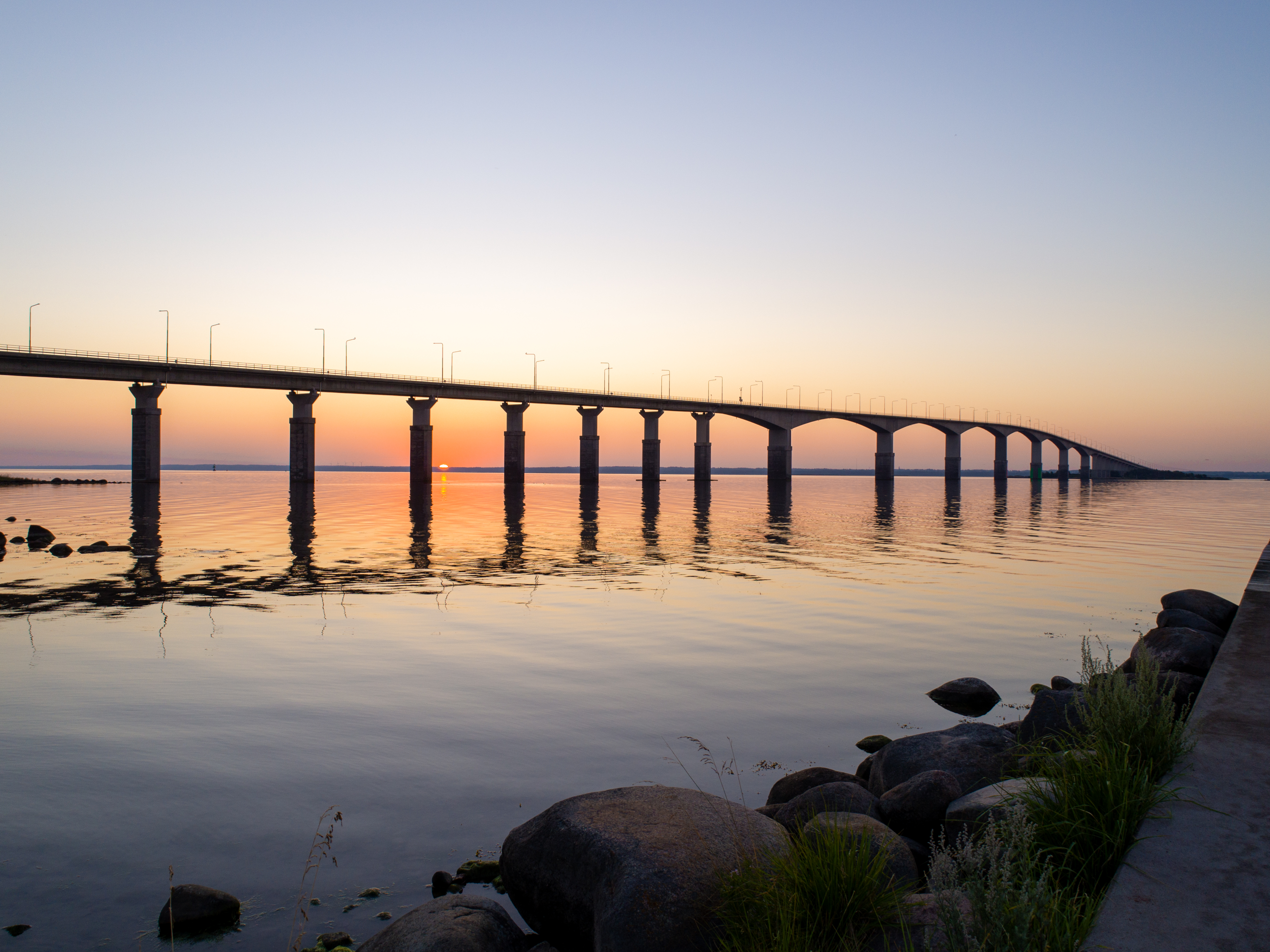 Ölandsbron vid solnedgång med mjukt ljus som speglas i det stilla vattnet, lång broförbindelse mellan Kalmar och Öland i Sverige.